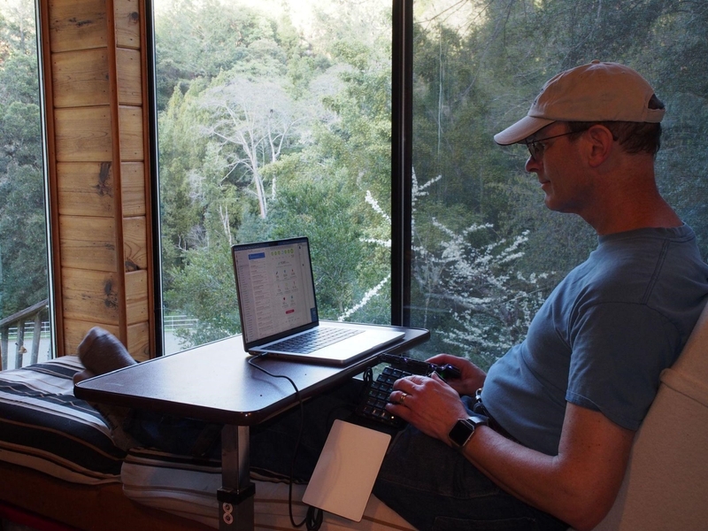 Eben Haber sits with his legs stretched in front of him, a notebook PC on a lap desk, and his Voyager on his lap. A beautiful forest view lies just outside the window.