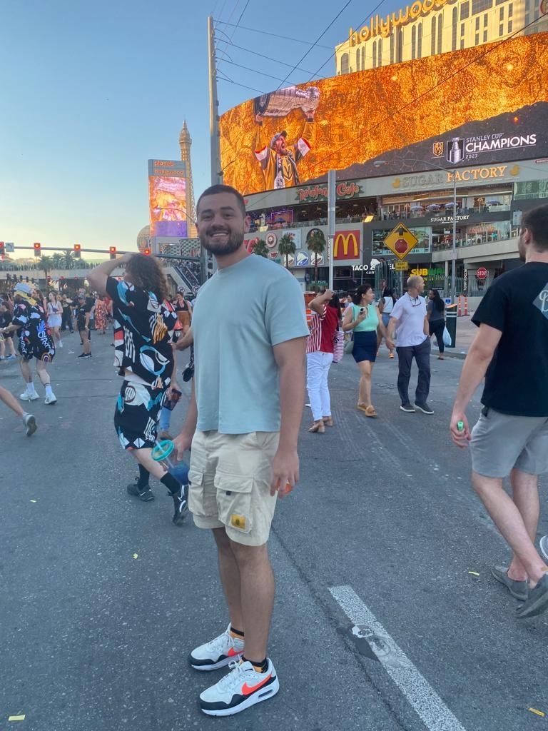 Andres Diaz full photo: A smiling man with very short hair and beard stands in a street during what appears to be a festival